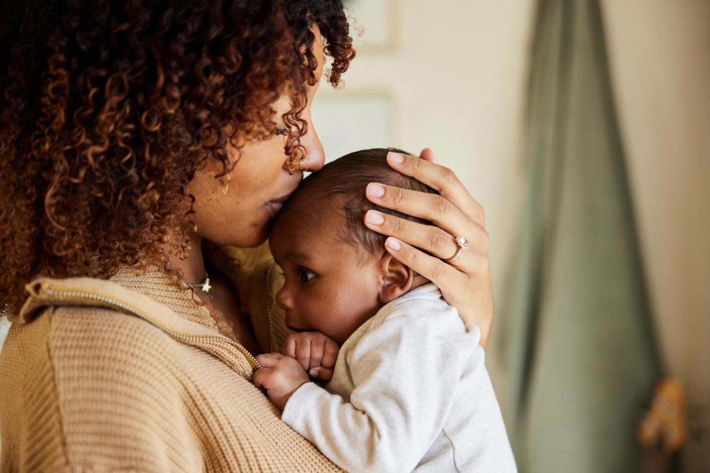 woman cradling baby child and kissing their forehead