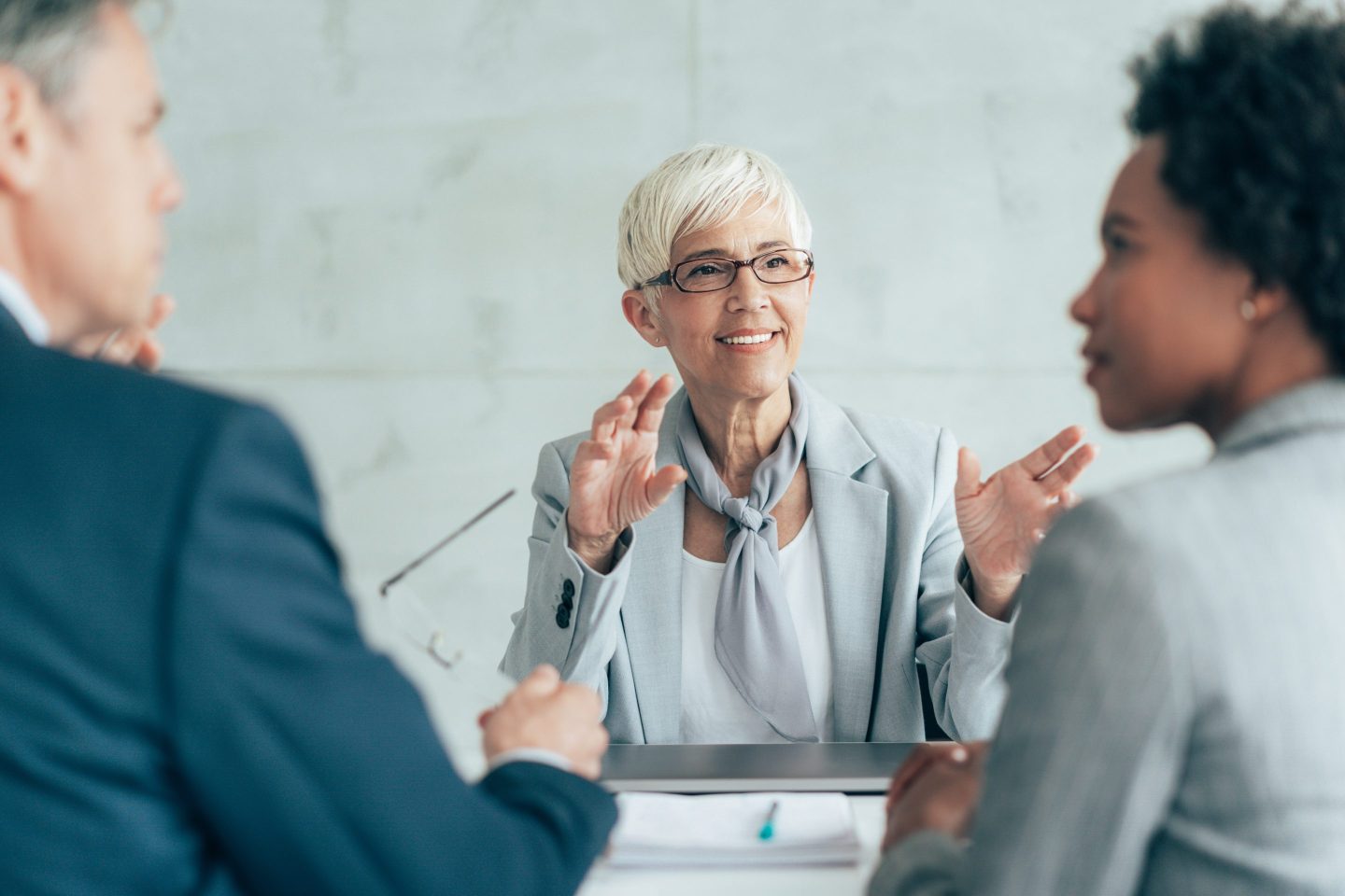 Group of businesspeople discuss, with a white-haired woman in the middle