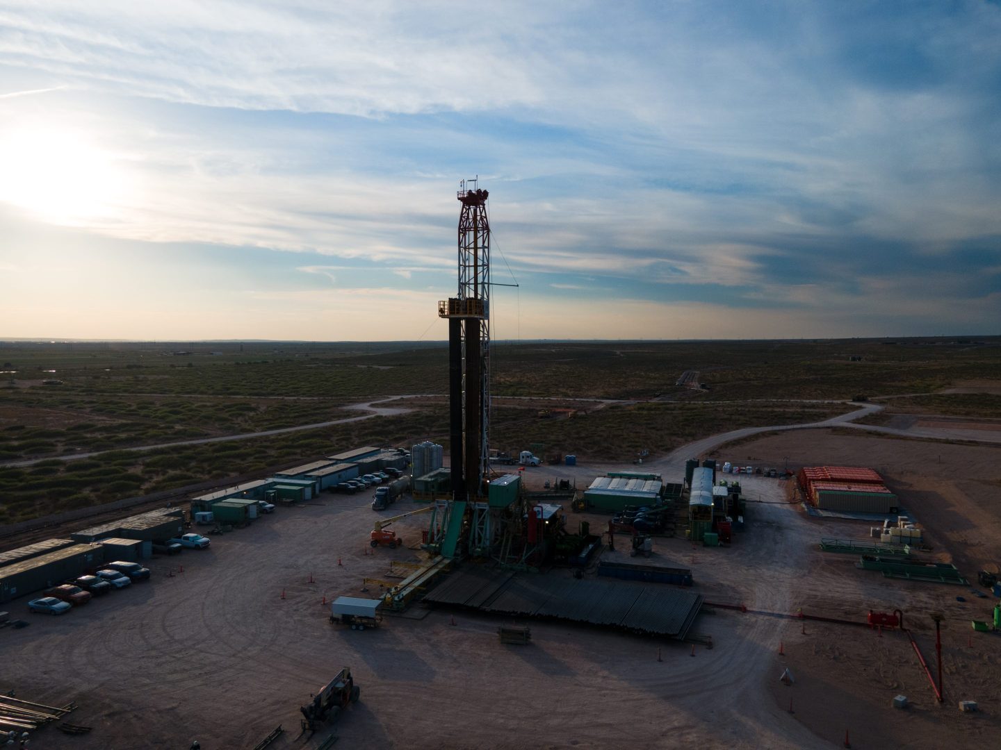 A drilling rig is pictured at an oil well site in the Permian Basin with trucks of workers and equipment lined up.