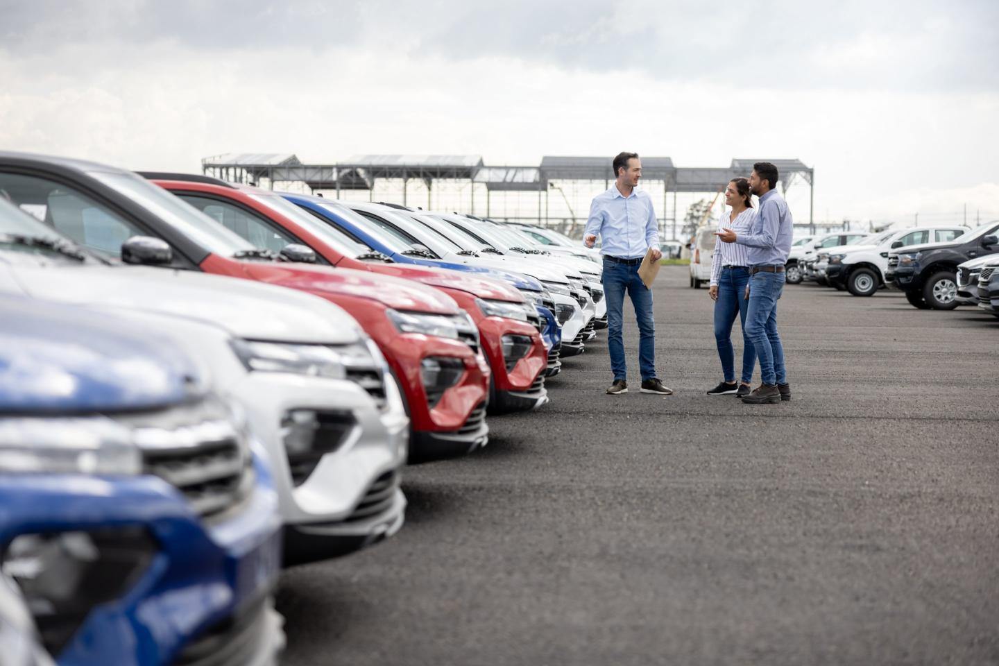 Happy salesman showing cars to a couple at the dealership