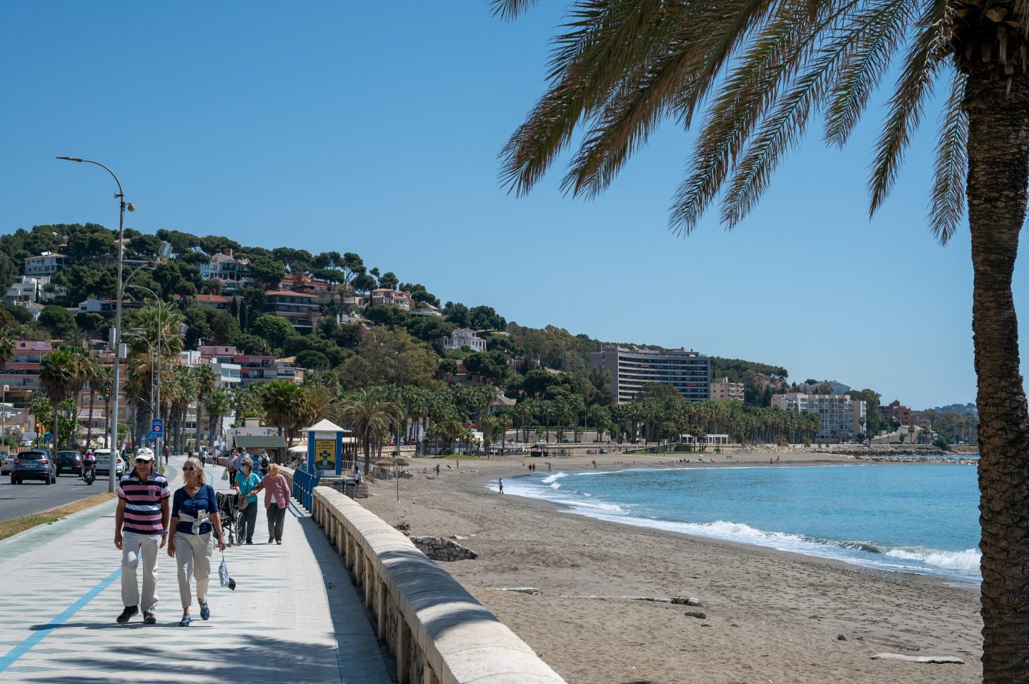 People walk along the promenade by Playa La Caleta beach on a sunny clear blue sky day on April 20, 2023 in Malaga, Spain.