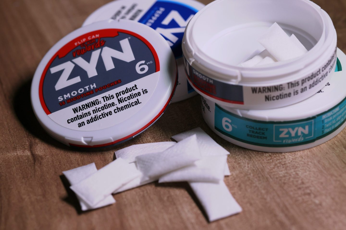 Plastic Zyn cans are stacked on top of each other, with some small white pouches piled next to them