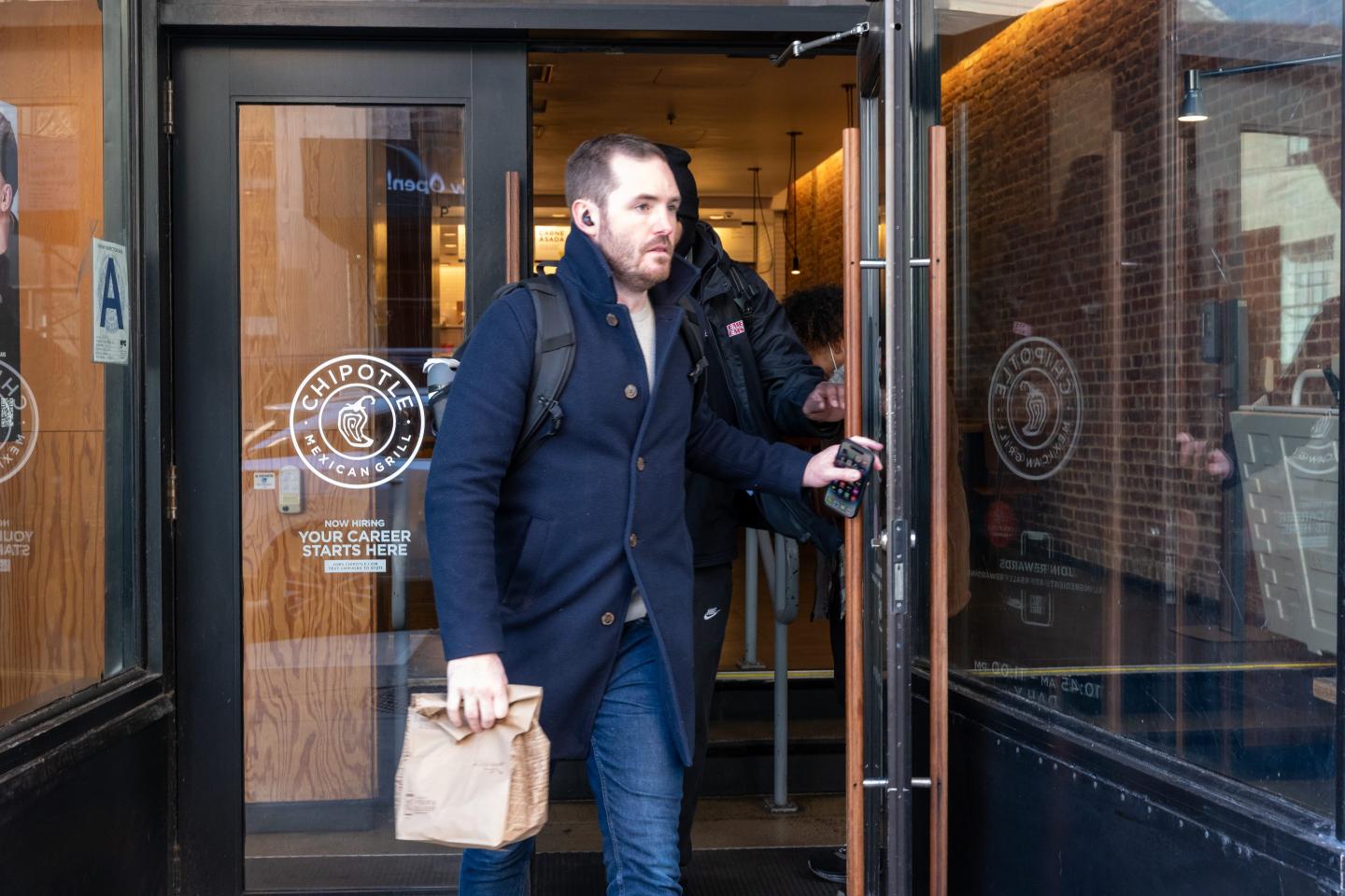 A man with a brown paper bag walks out of a Chipotle store.