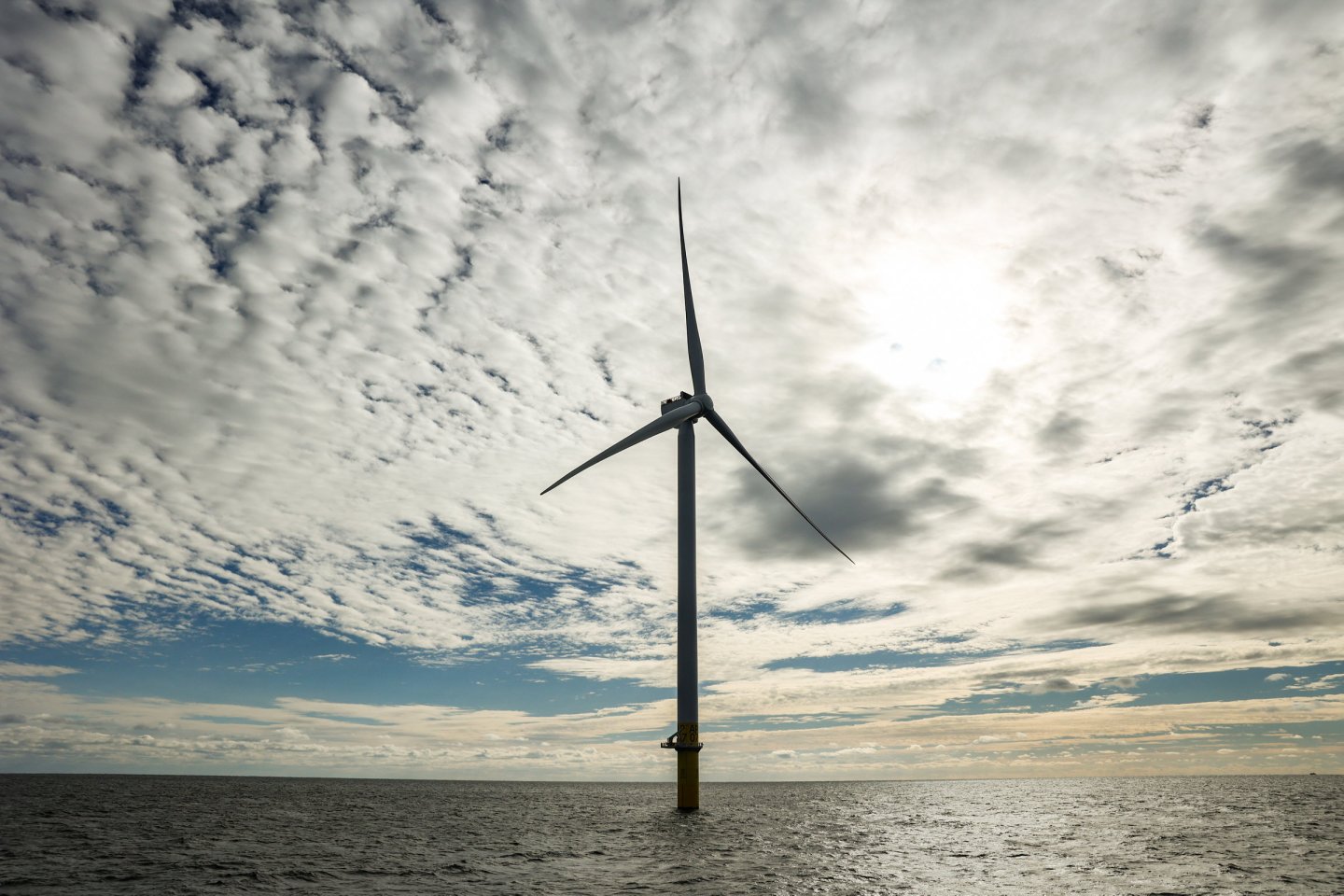 A wind turbine offshore of New York is pictured with clouds in the background.