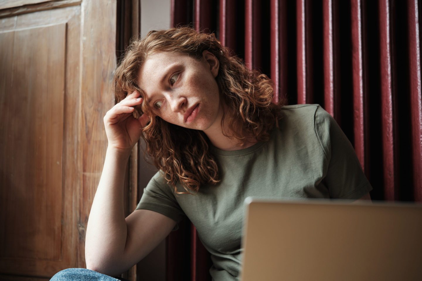 Young woman leans her head on her hand with a laptop in front of her