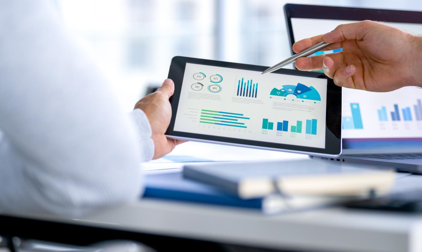 office workers looking at financial data, charts, and graphs on a digital tablet and a laptop computer