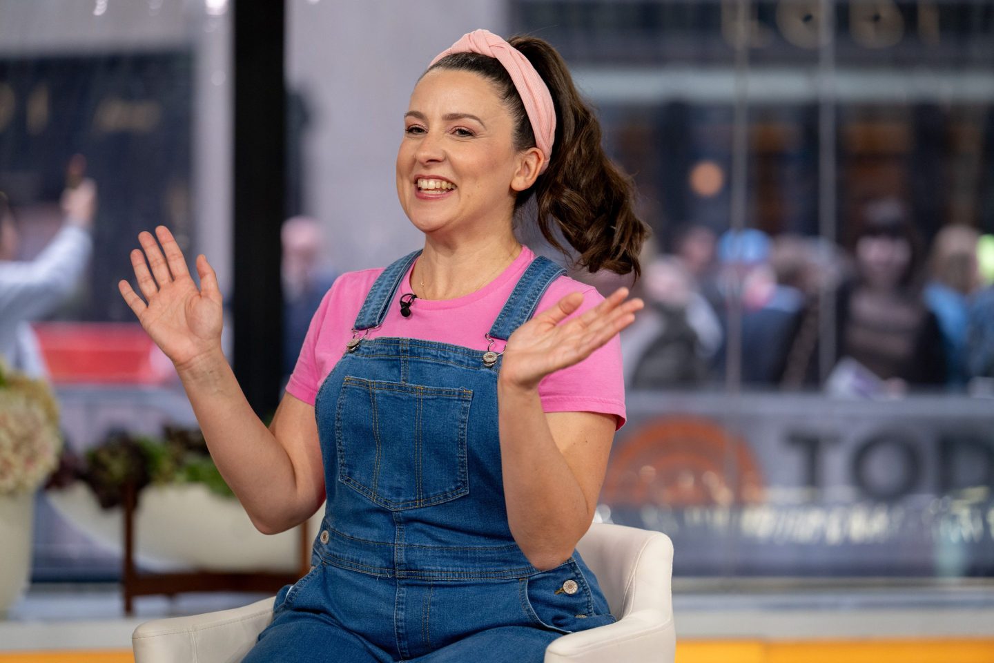 Ms. Rachel with her hands up, wearing blue overalls and pink t-shirt