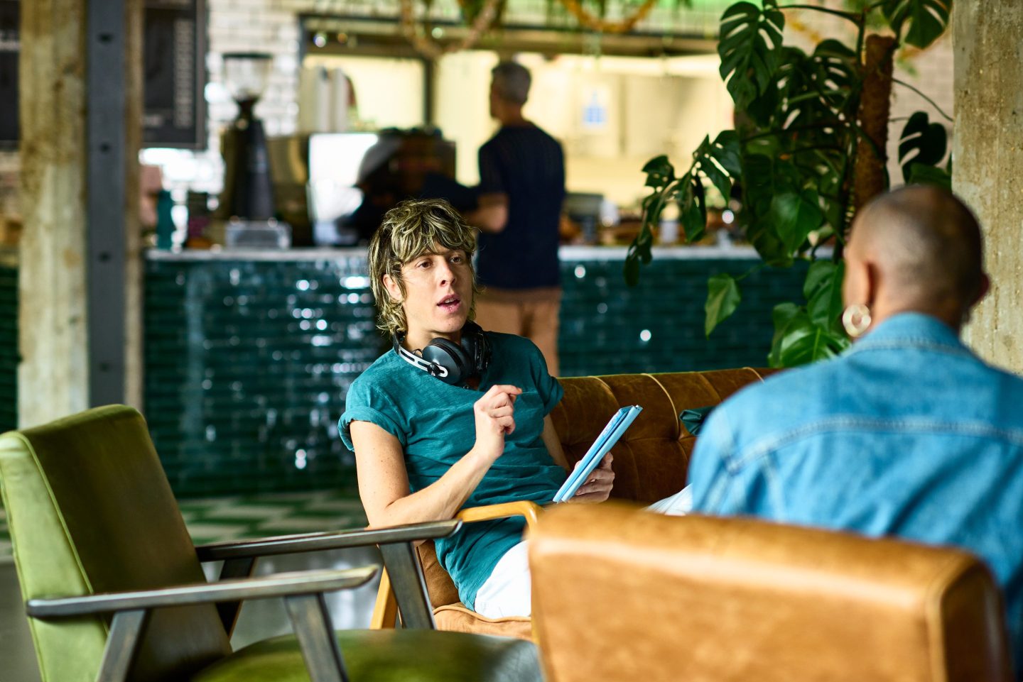 Mid adult woman and non binary co-worker sitting in cafe for one-to-one, woman holding tablet, talking and explaining