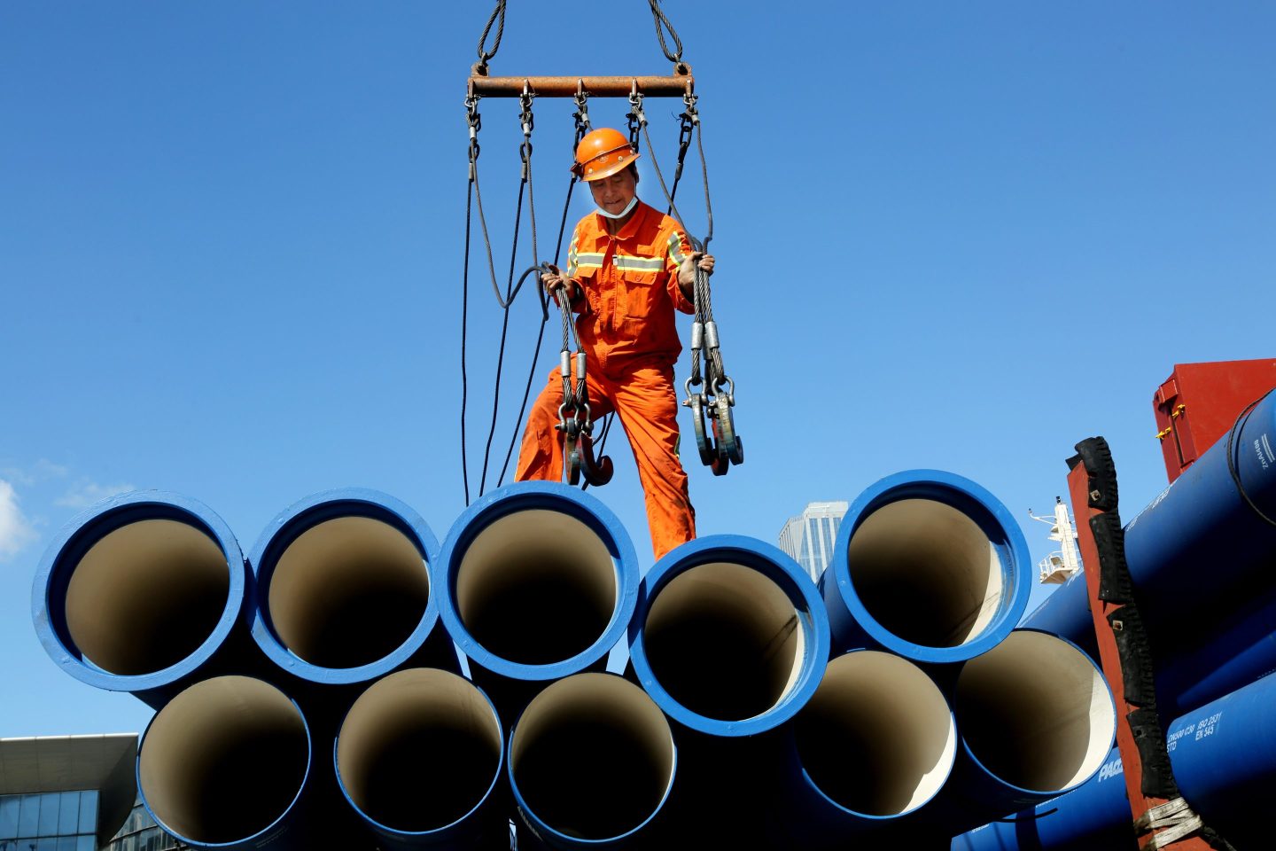 A dock worker stands on top of several large tubes.
