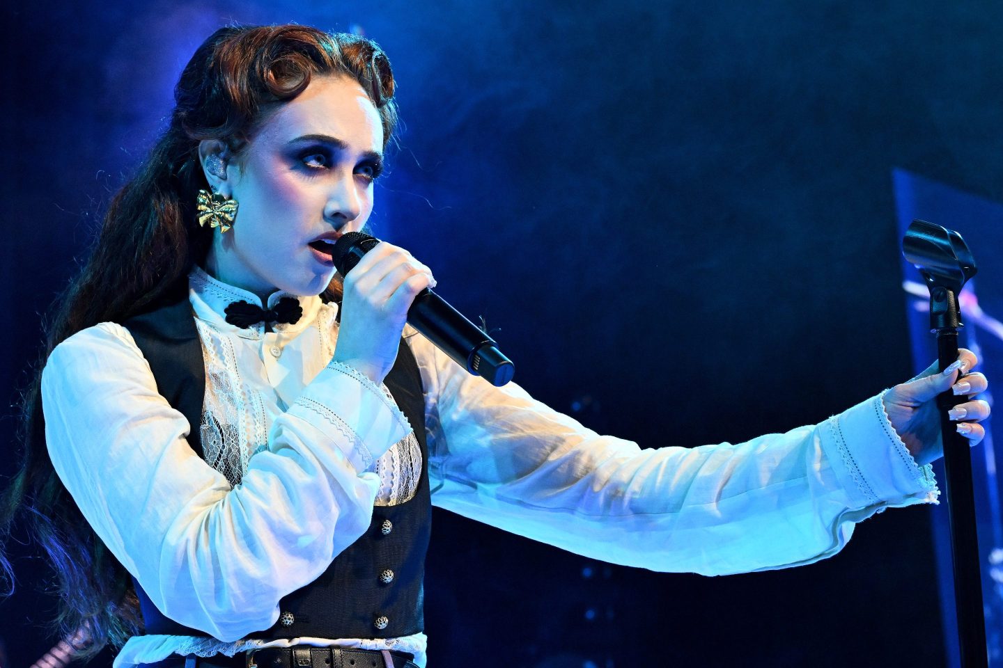 Closeup of Chappell Roan holding a microphone in blue light