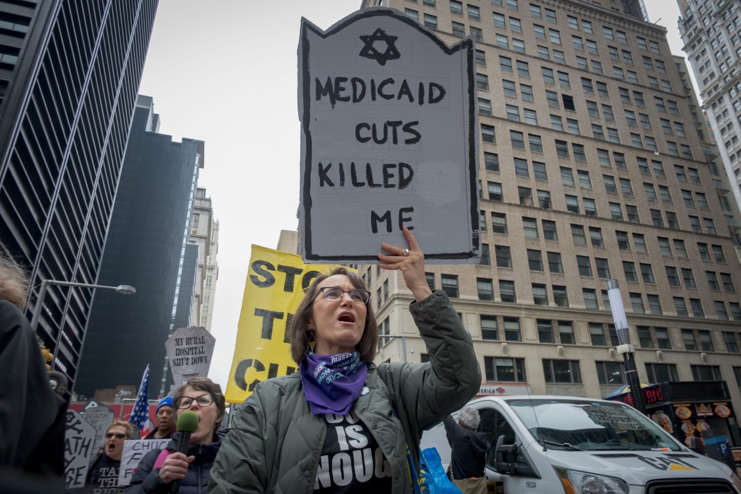 Woman holds a sign reading "medicaid cuts killed me" at a protest