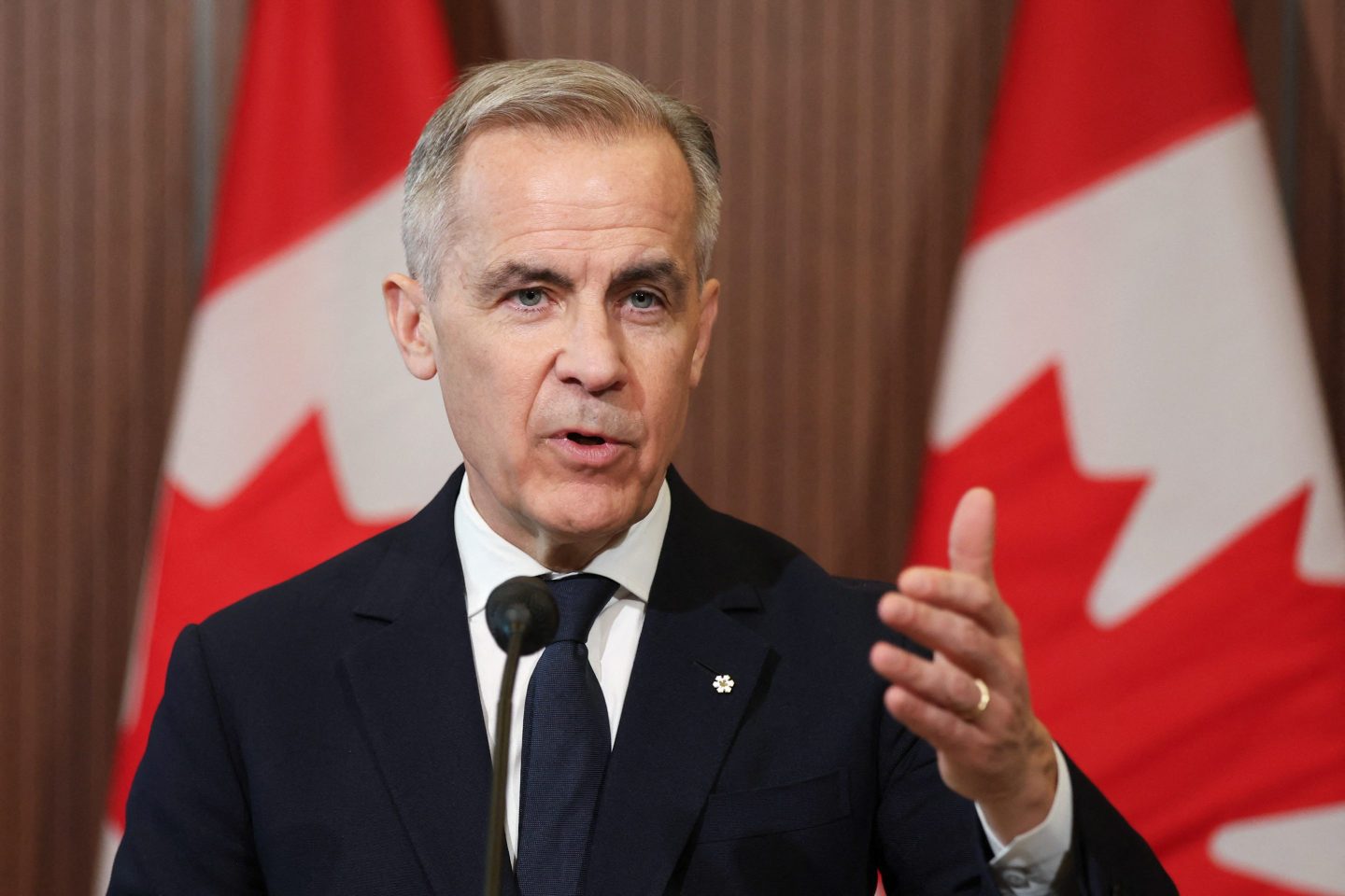 Mark Carney stands in front of two Canadian flags