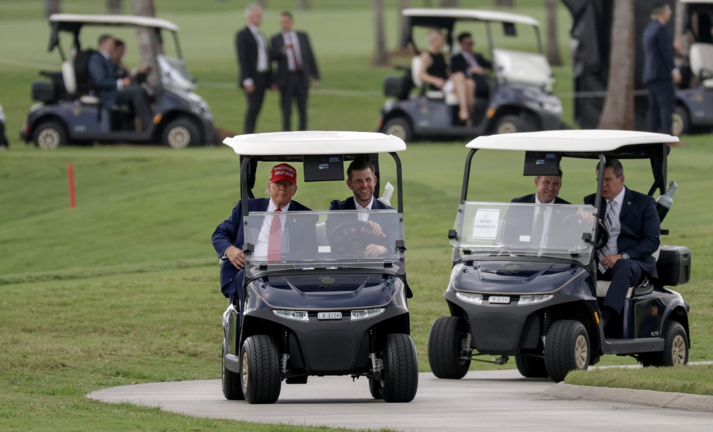 Donald and Eric Trump ride in a golf cart surrounded by Secret Service in golf carts