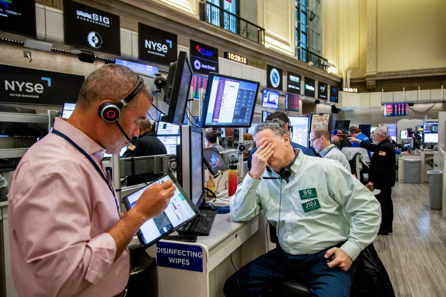 A man puts his hand to his face as he swivels his chair away from his monitors on the floor of the New York Stock Exchange.