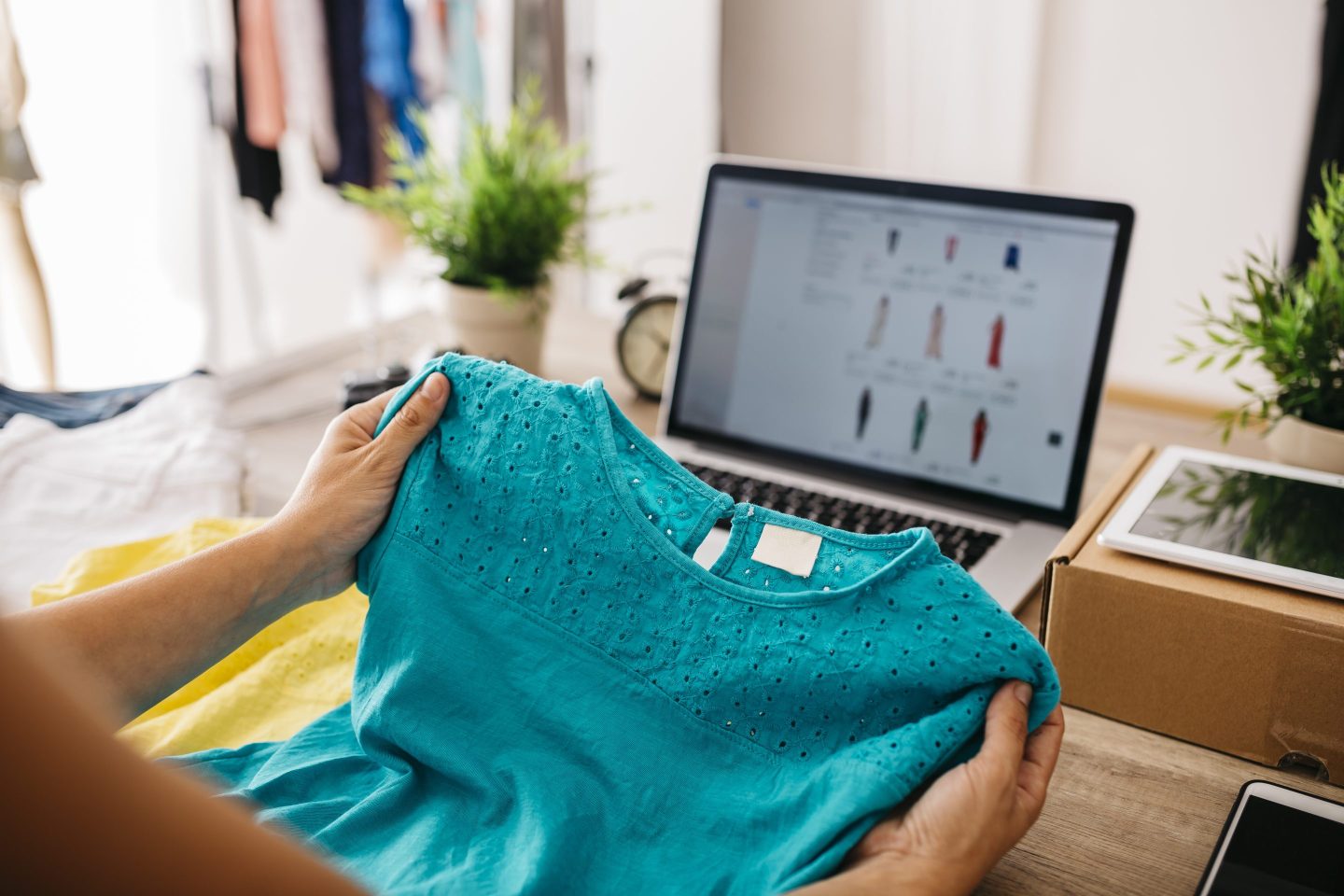 Hands hold a blouse in front of a laptop