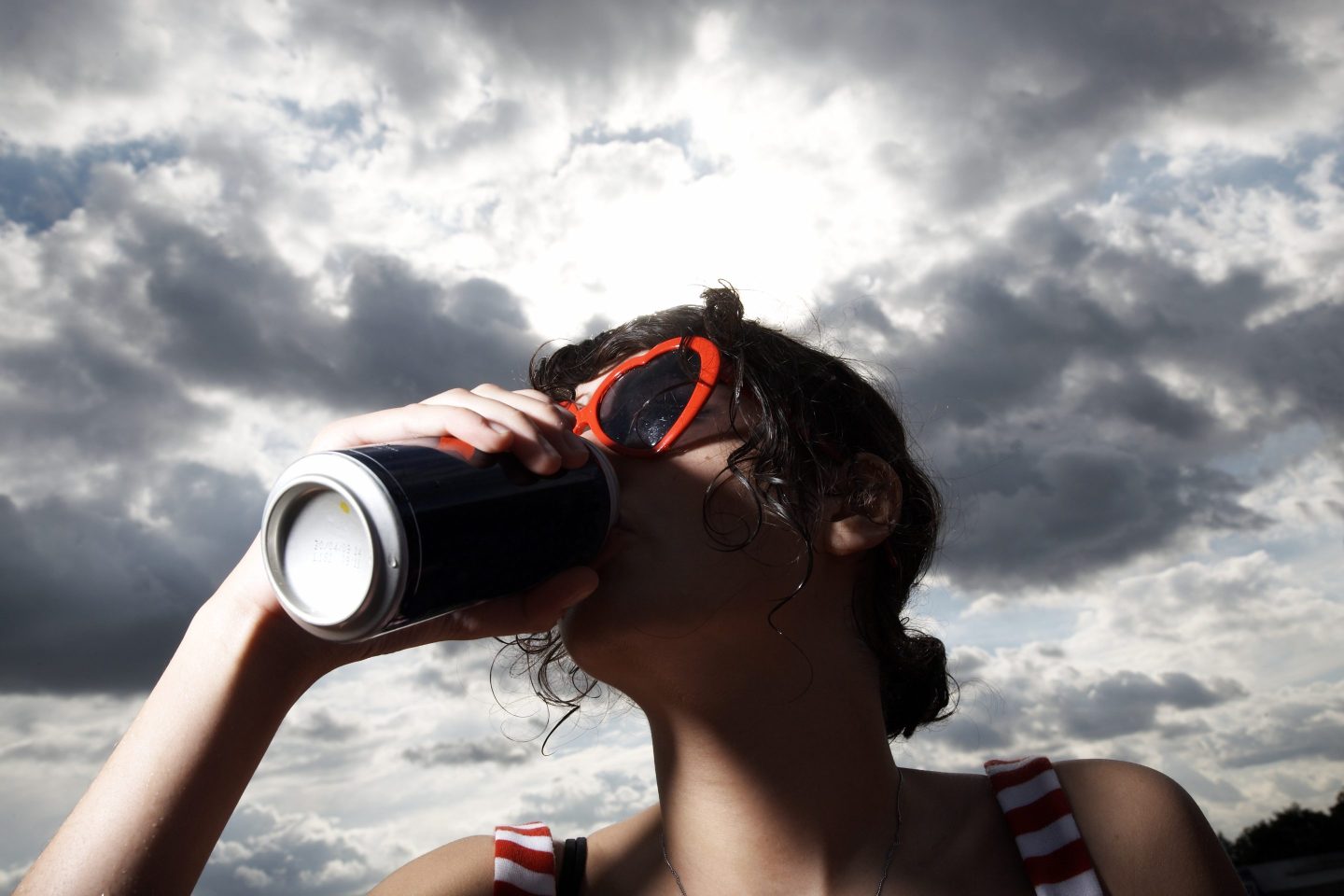 Close-up of a woman wearing red framed sunglasses drinking from a can