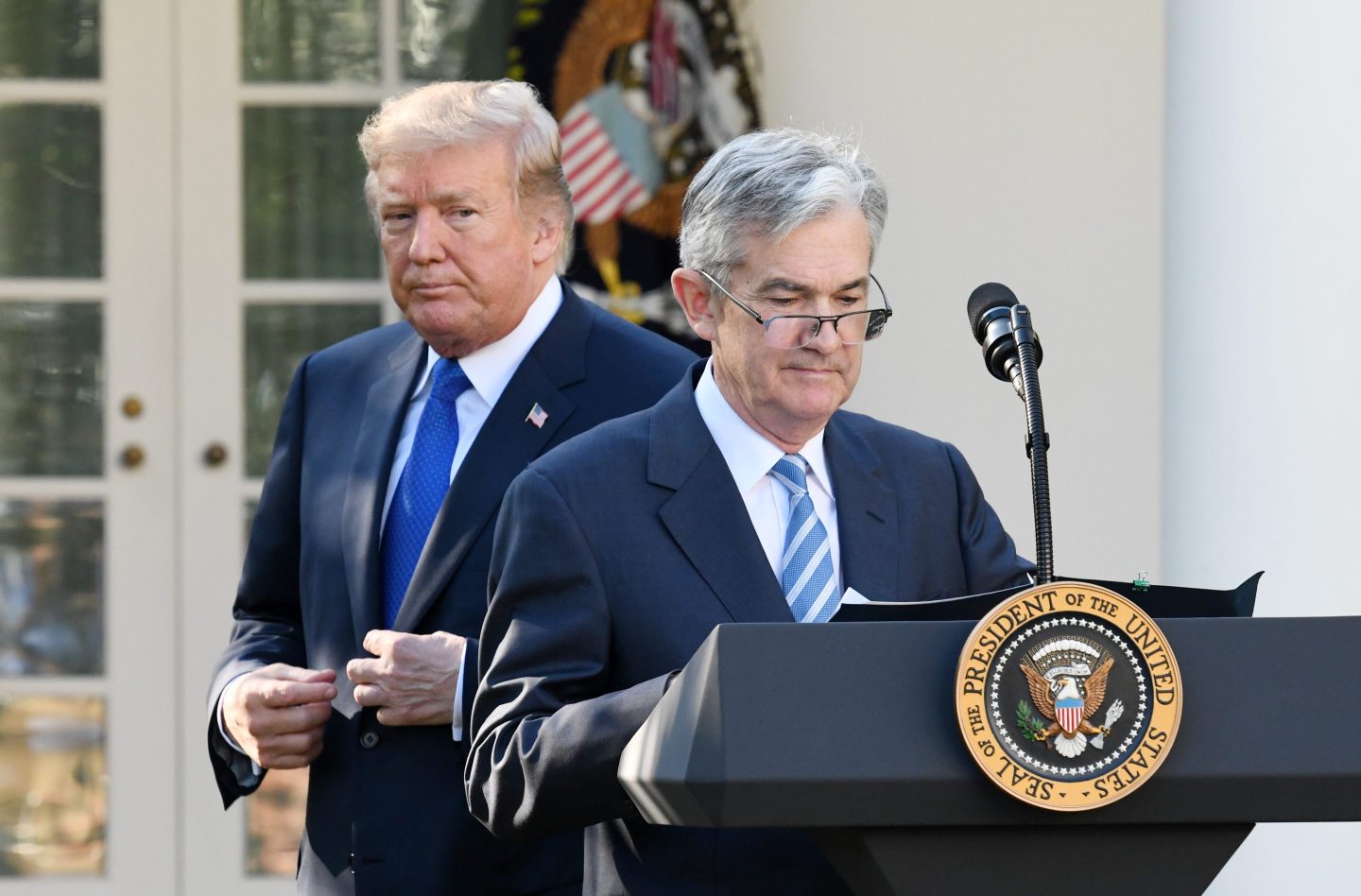 President Donald Trump walks behind Jerome Powell, who pauses while speaking at a podium during his nomination announcement in the White House Rose Garden.