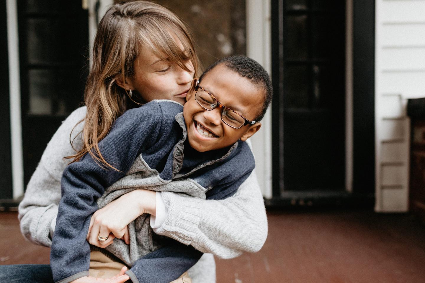 A mom is hugging her son from behind