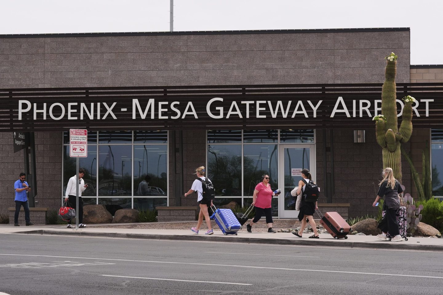 Passengers walk in front of Mesa Gateway Airport, where Avelo Airlines started making deportation flights on behalf of the federal government on Monday, May 12, 2025, in Mesa, Ariz.