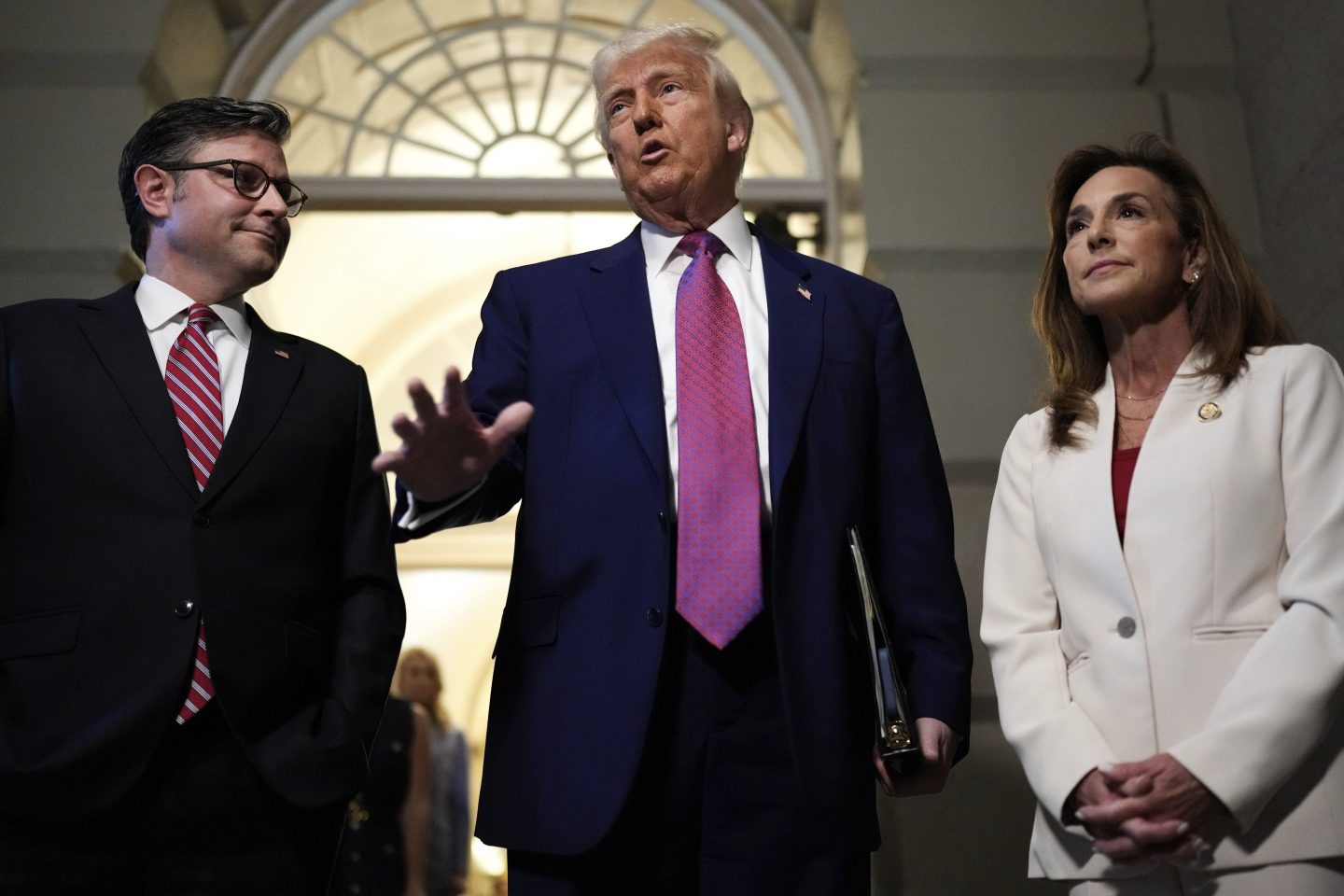 President Donald Trump, center, surrounded by Speaker of the House Mike Johnson, R-La., and Rep. Lisa McClain, R-Mich., speaks to reporters before a House Republican conference meeting, on May 20, 2025, at the U.S. Capitol in Washington.