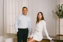 Tarang Amin and Hailey Bieber lean on a glass table and look forward.