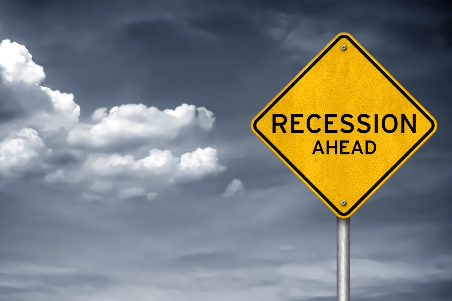 Storm clouds hang in the sky behind a sign that reads "recession ahead"