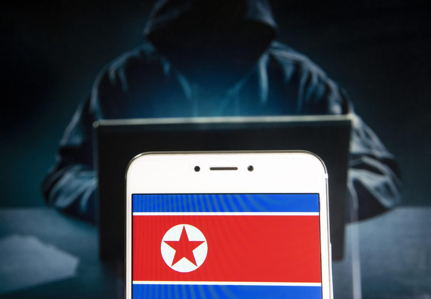 Photo illustration of the North Korean flag seen on a screen with the image of a hacker behind it