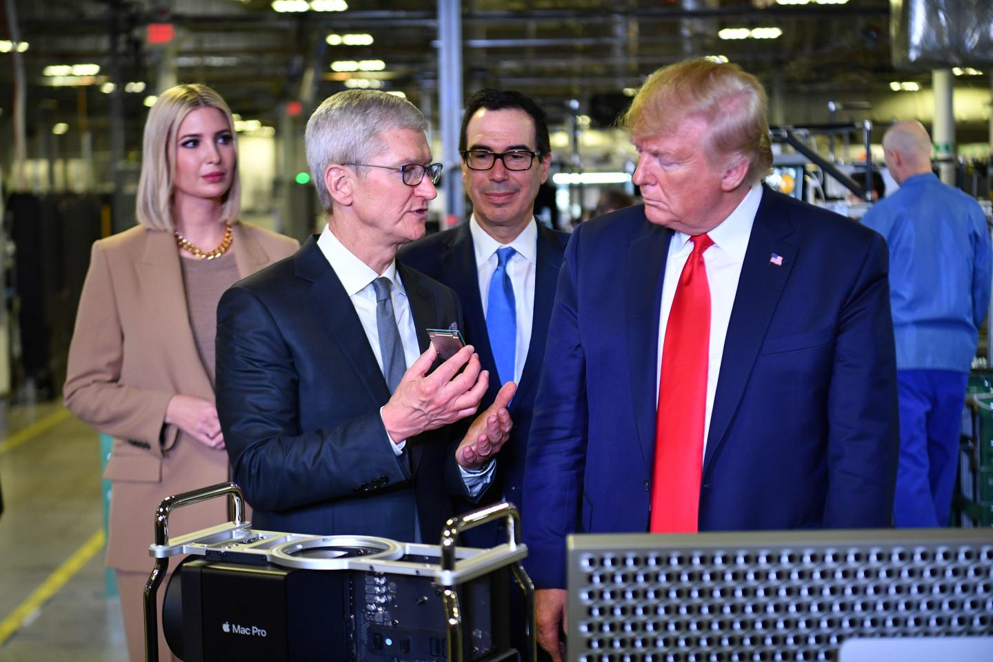 Tim Cook shows Donald Trump a piece of technology while standing in a factory.