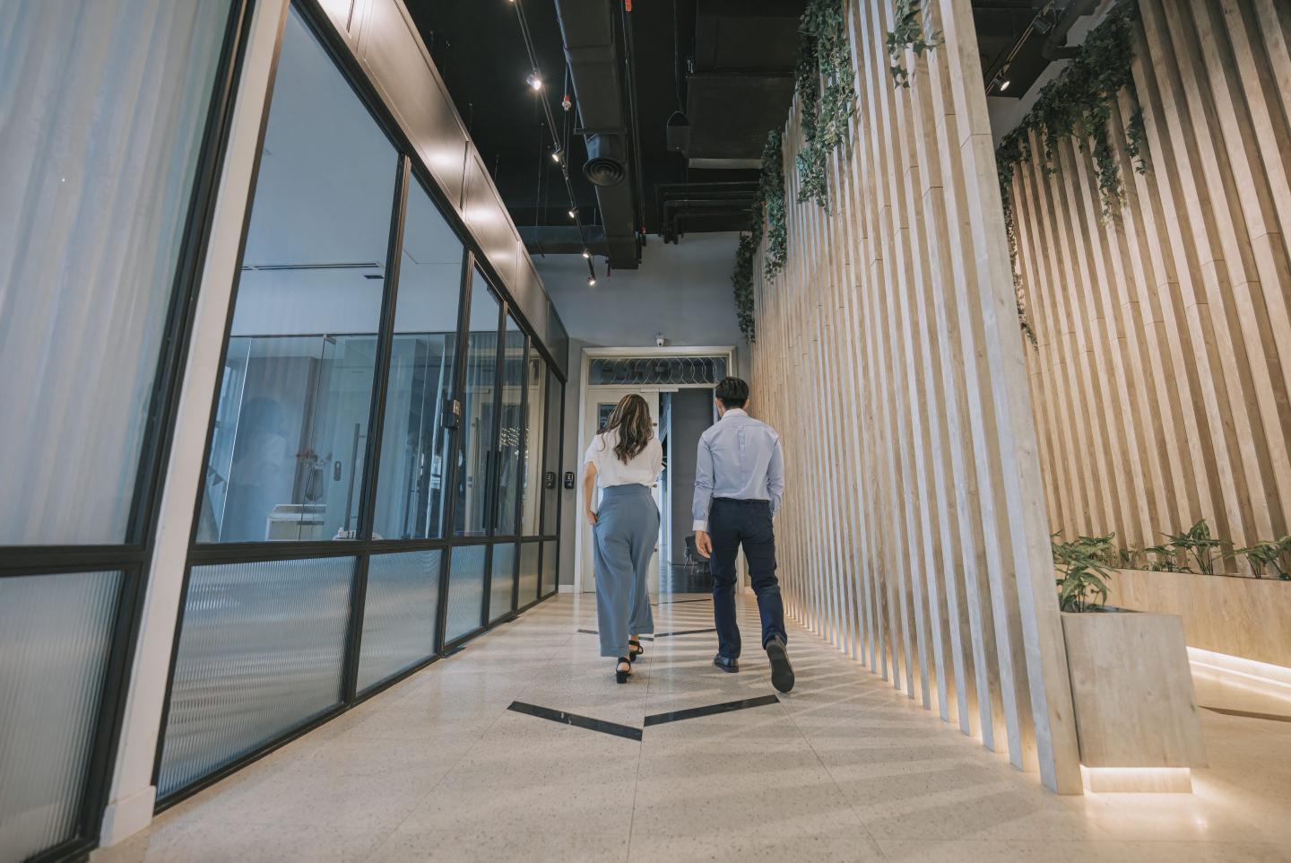 Two colleagues walking in corridor on the way out of an office.