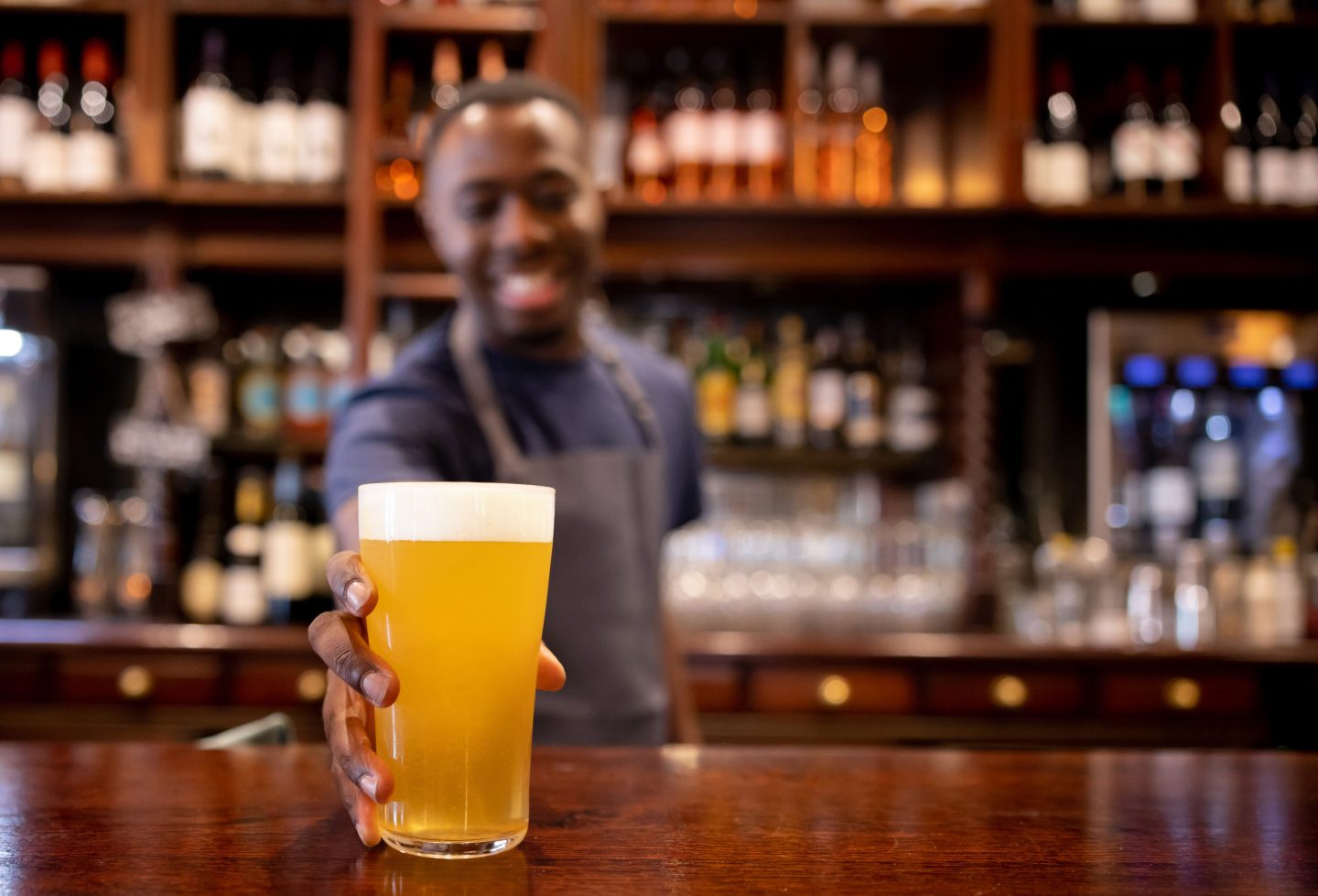 Male bartender, in background, serving up a pint of beer, in foreground