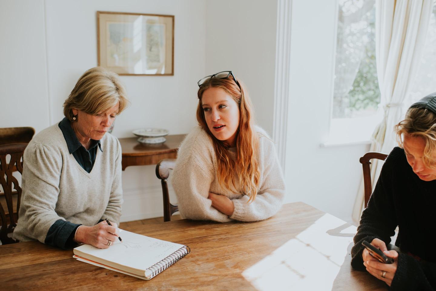 senior and young woman sitting at a table, drafting a document and conversing