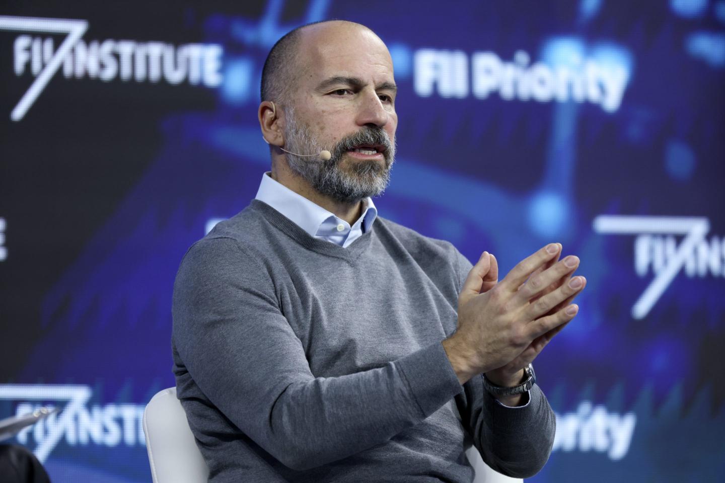 Dara Khosrowshahi speaks on stage and holds his palms in front of him, pressed together.