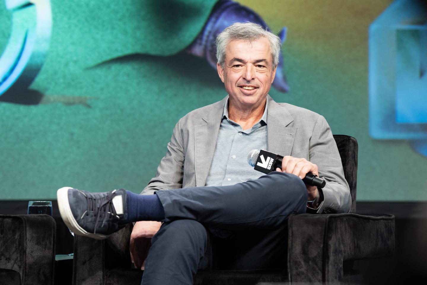 Eddy Cue sits on stage with his legs crossed, holding a microphone.