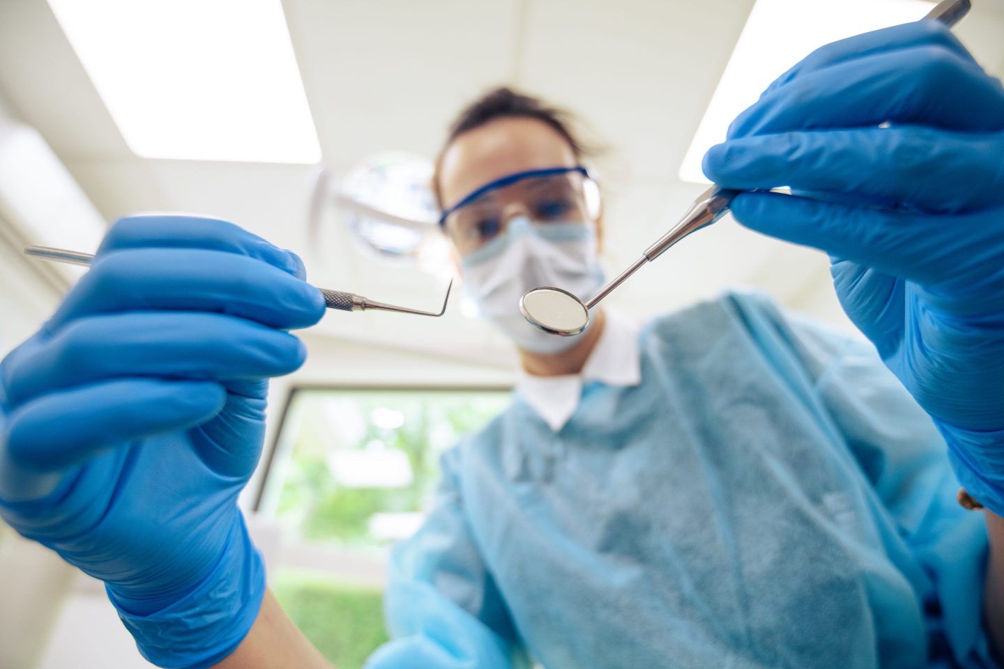 Patient's view of masked dentist approaching with tools in hands