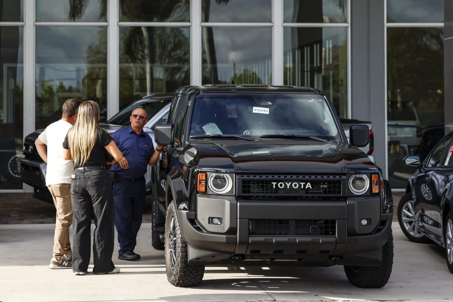 A car dealer shows prospective buyers a Toyota truck in a dealership lot.