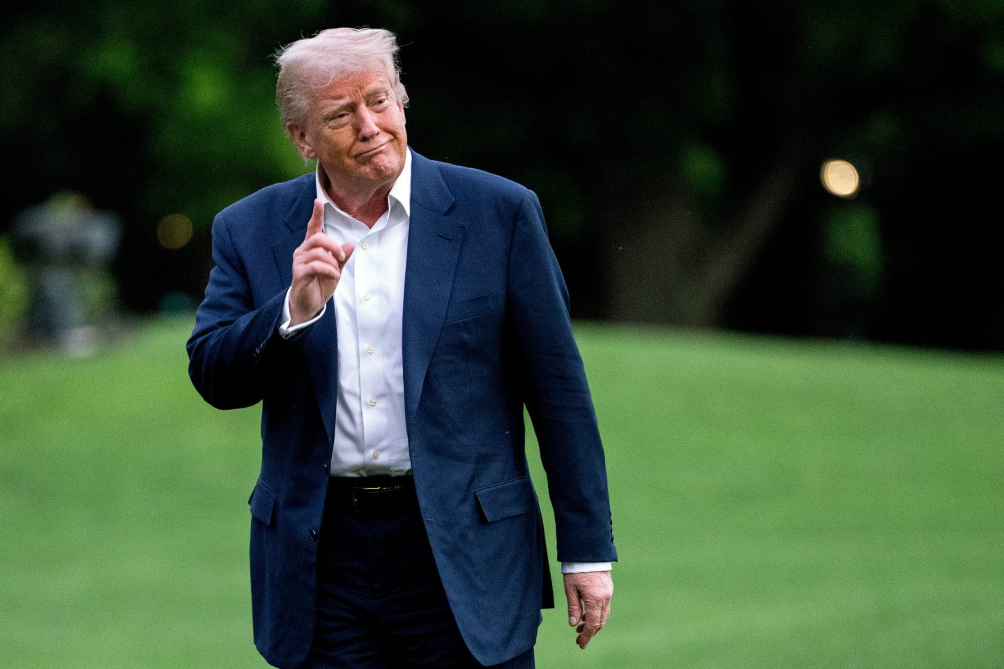 Donald Trump, walking on grass, points his index finger in the air.