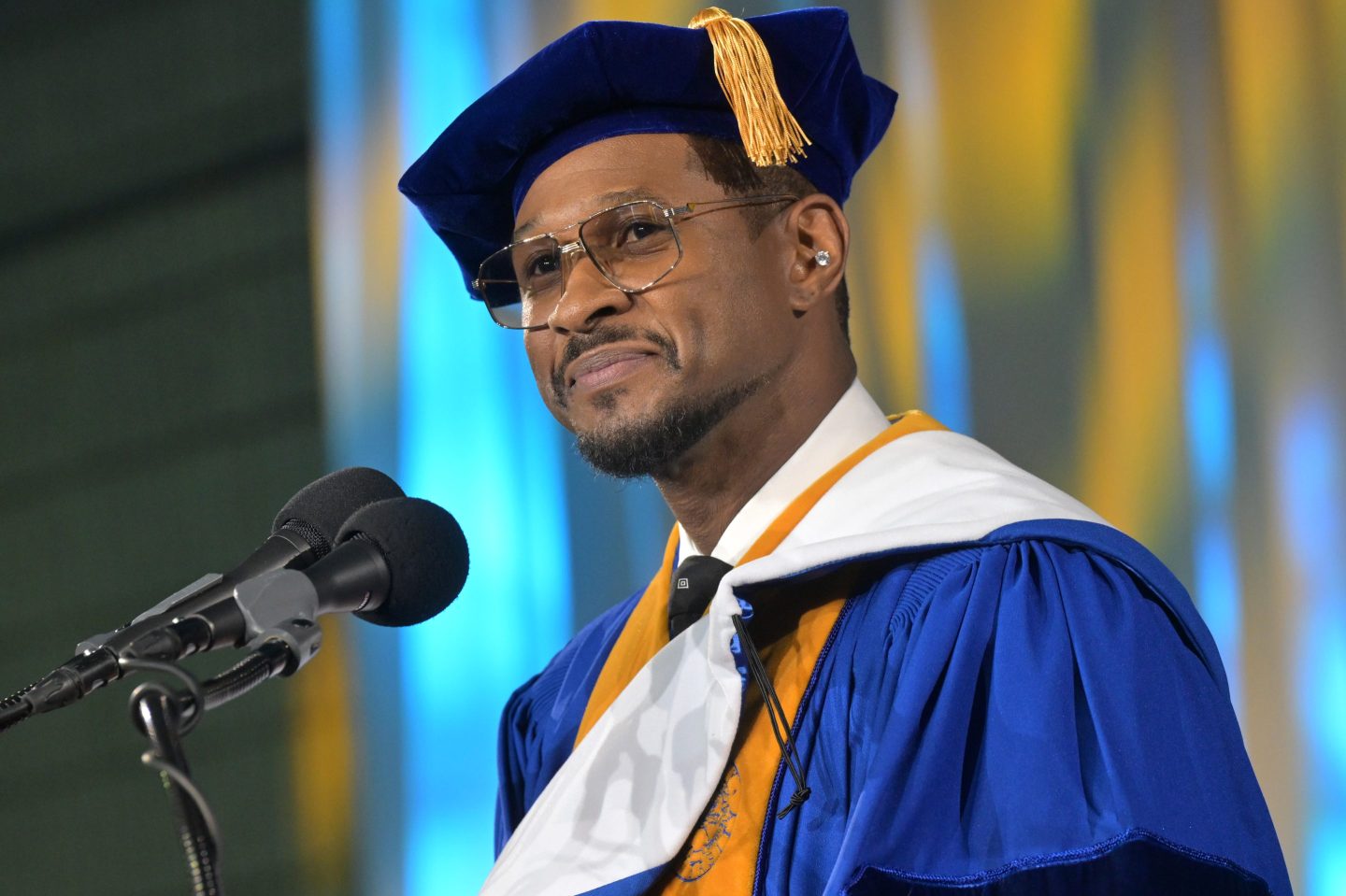 Usher wearing graduation regalia in front of a microphone