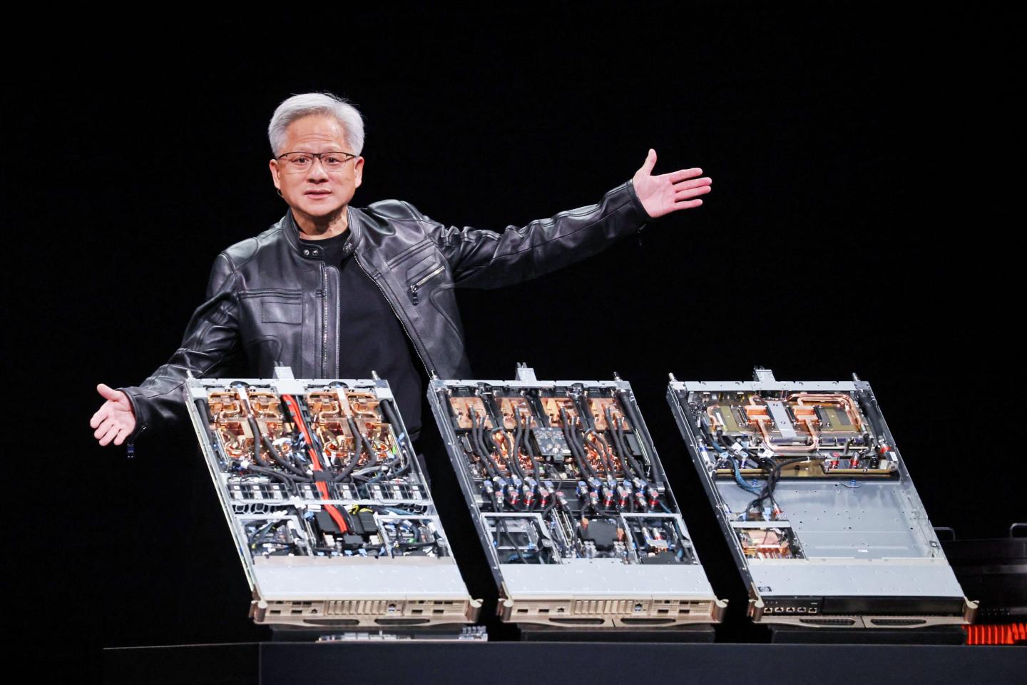 Jensen Huang spreads his hands over a display of giant computer chips as he gives a speech.