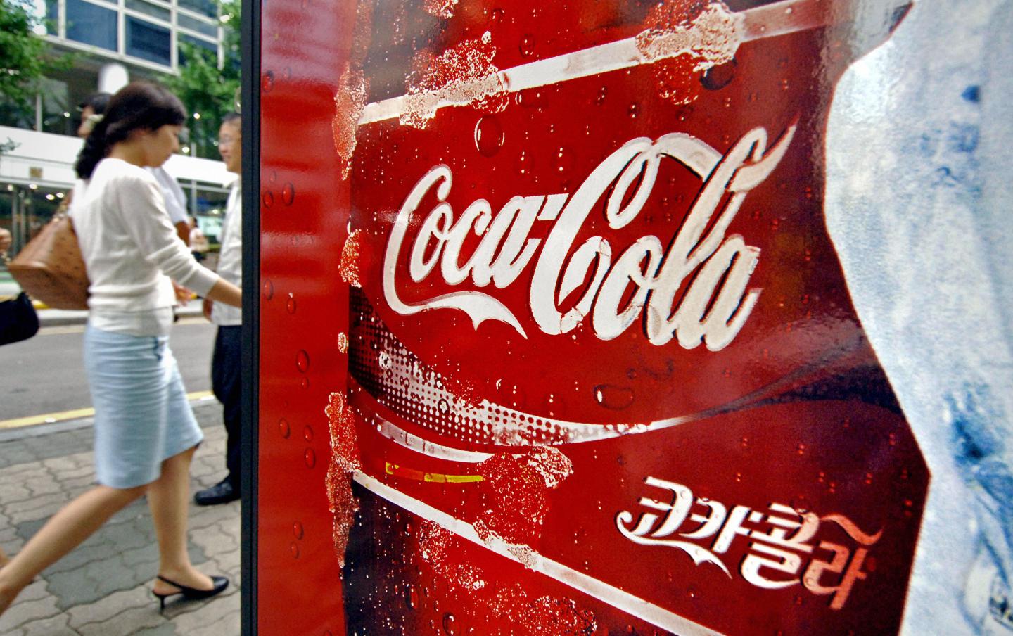 A woman walks past a Coca-Cola advert on the street.