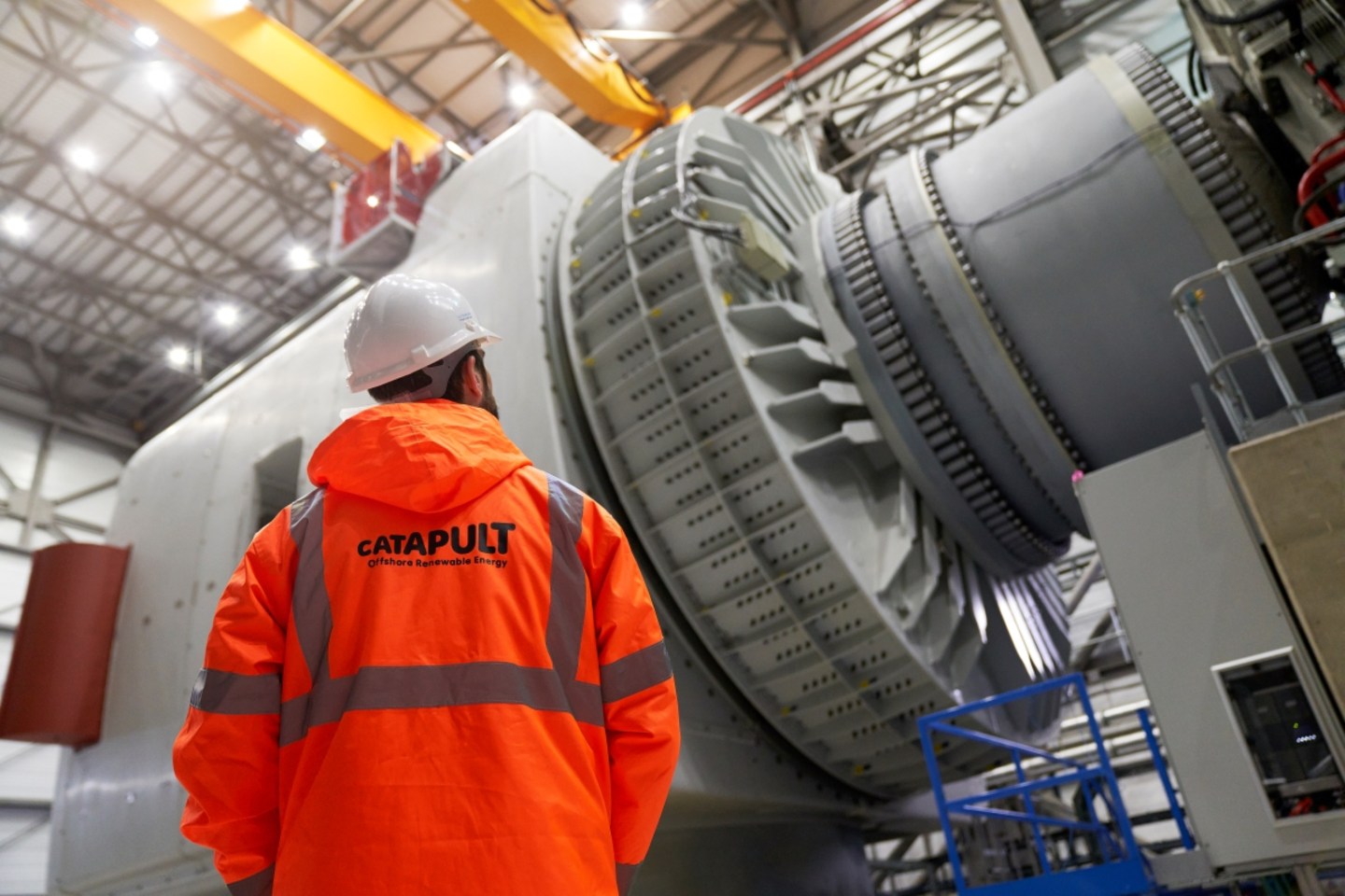 An engineer at ORE Catapult in Blyth, U.K., stands beneath the nacelle of an offshore wind turbine, which houses the turbine’s drivetrain.