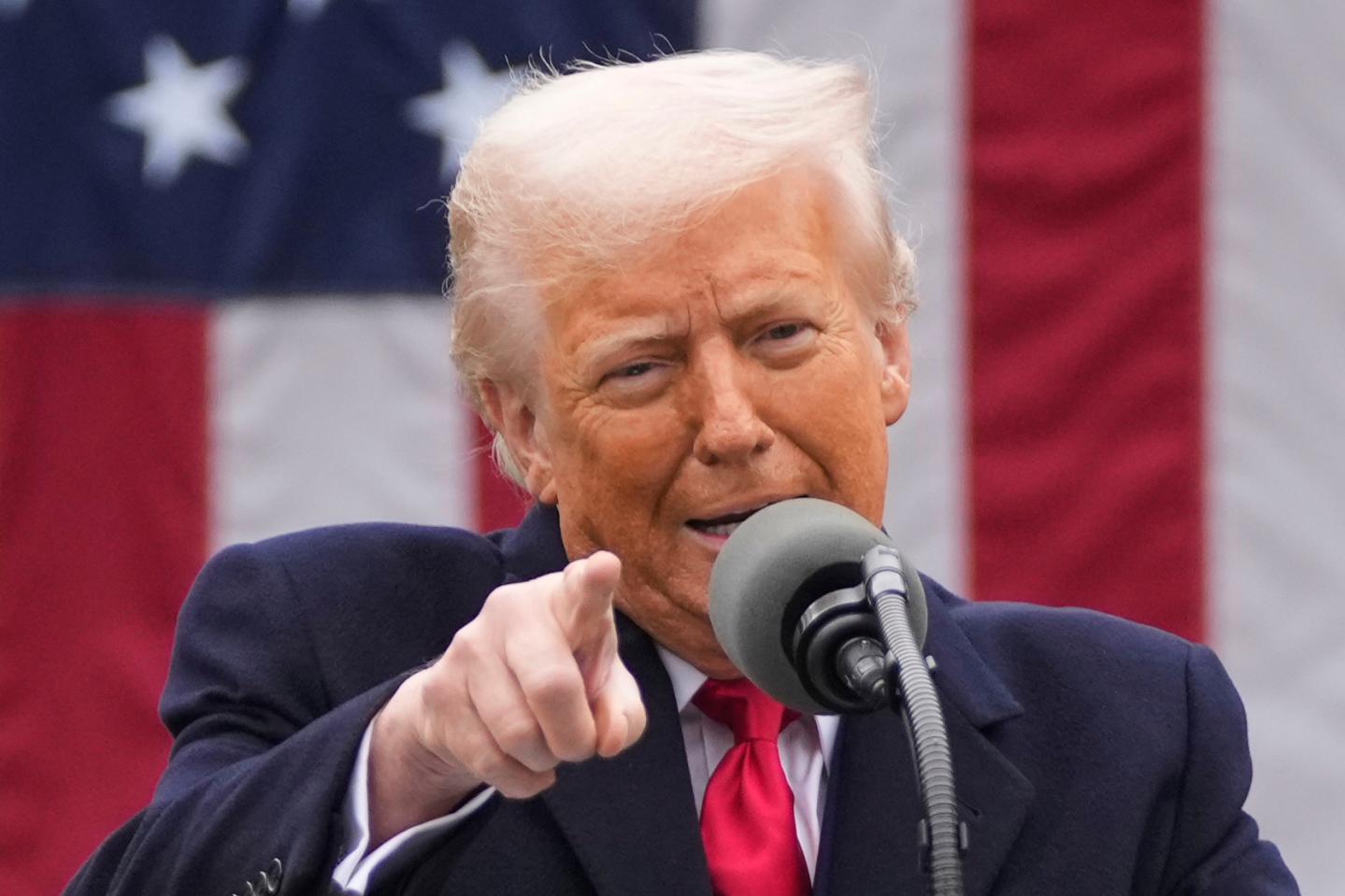 Trump speaks into a microphone and points into the crowd in front of an American flag