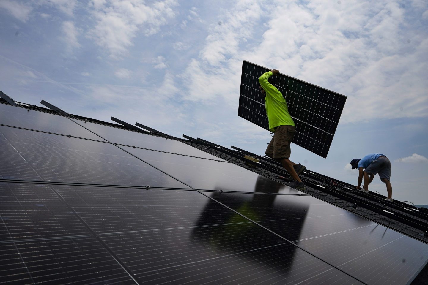 Nicholas Hartnett, owner of Pure Power Solar, carries a panel as he and Brian Hoeppner, right, install a solar array on the roof of a home in Frankfort, Ky., July 17, 2023.