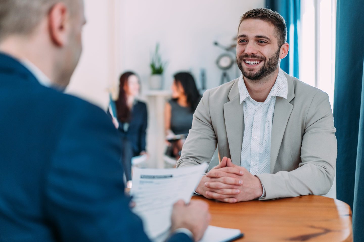 Shot of male HR manager looking through resume and asking young man questions about his skills and previous job experience.