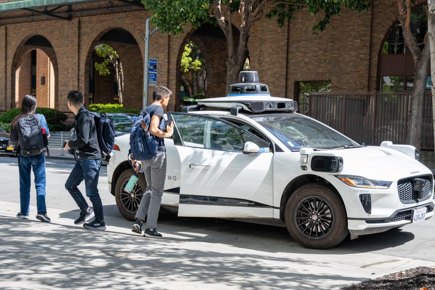 Students exit a Waymo car stopped on the street.