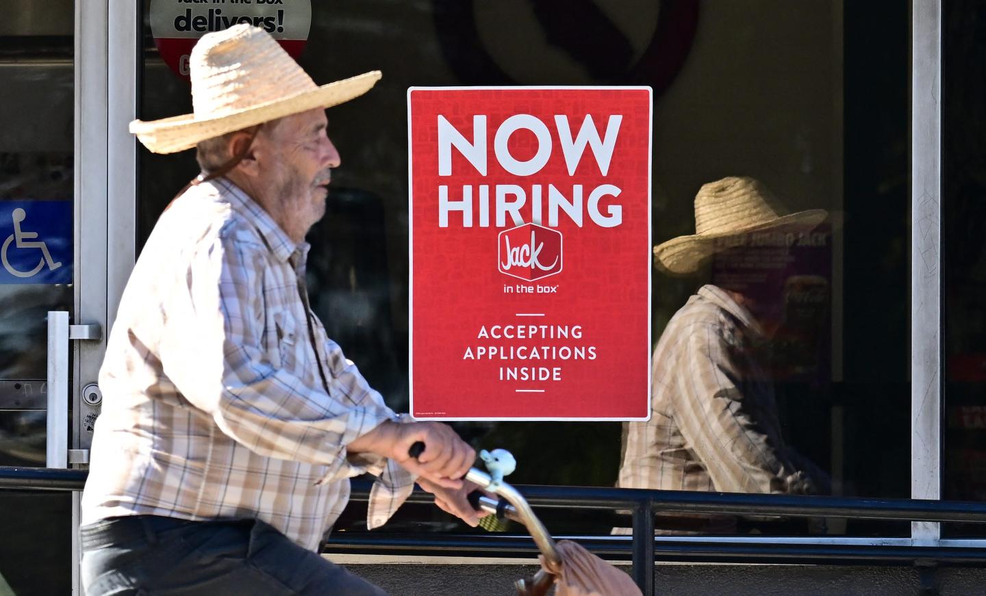 Man walking by a jack in the box with a "now hiring" sign