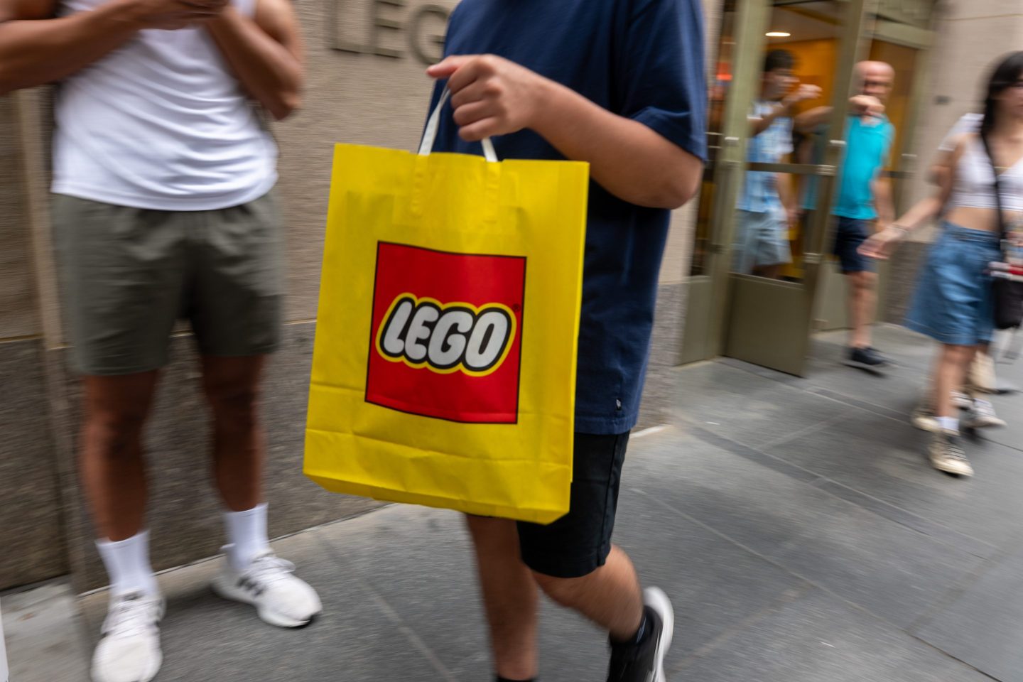 person carrying yellow and red Lego shopping back