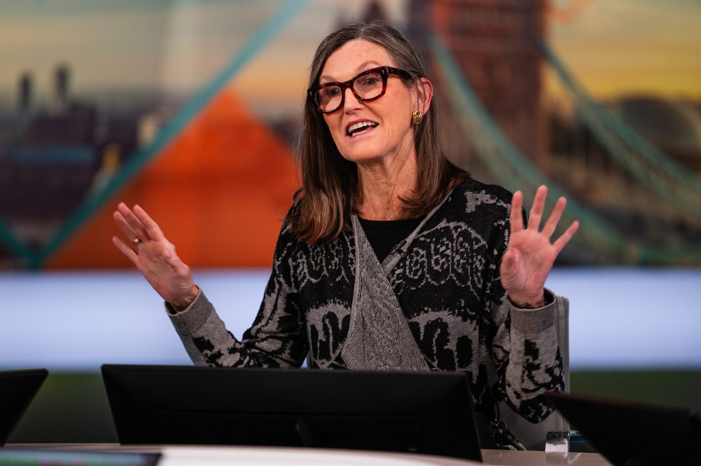Cathie Wood raises both her hands as she talks during a television interview.
