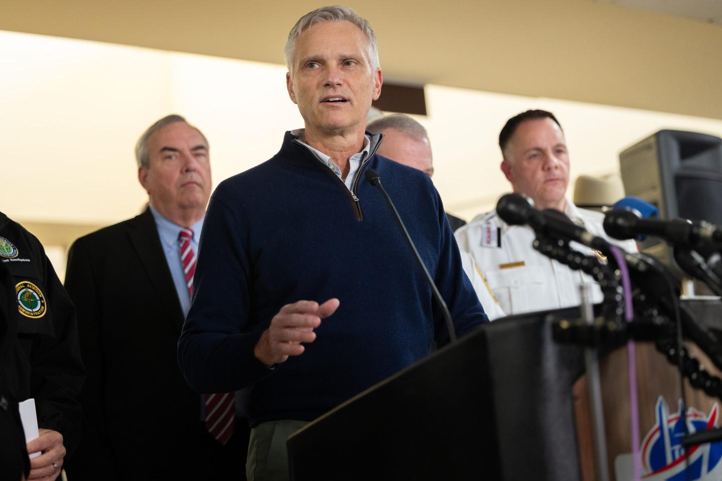 Robert Isom speaks at a podium while a group of people stand behind him.