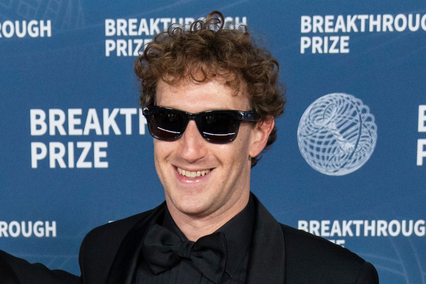 Mark Zuckerberg smiles wearing all black, with black sunglasses
