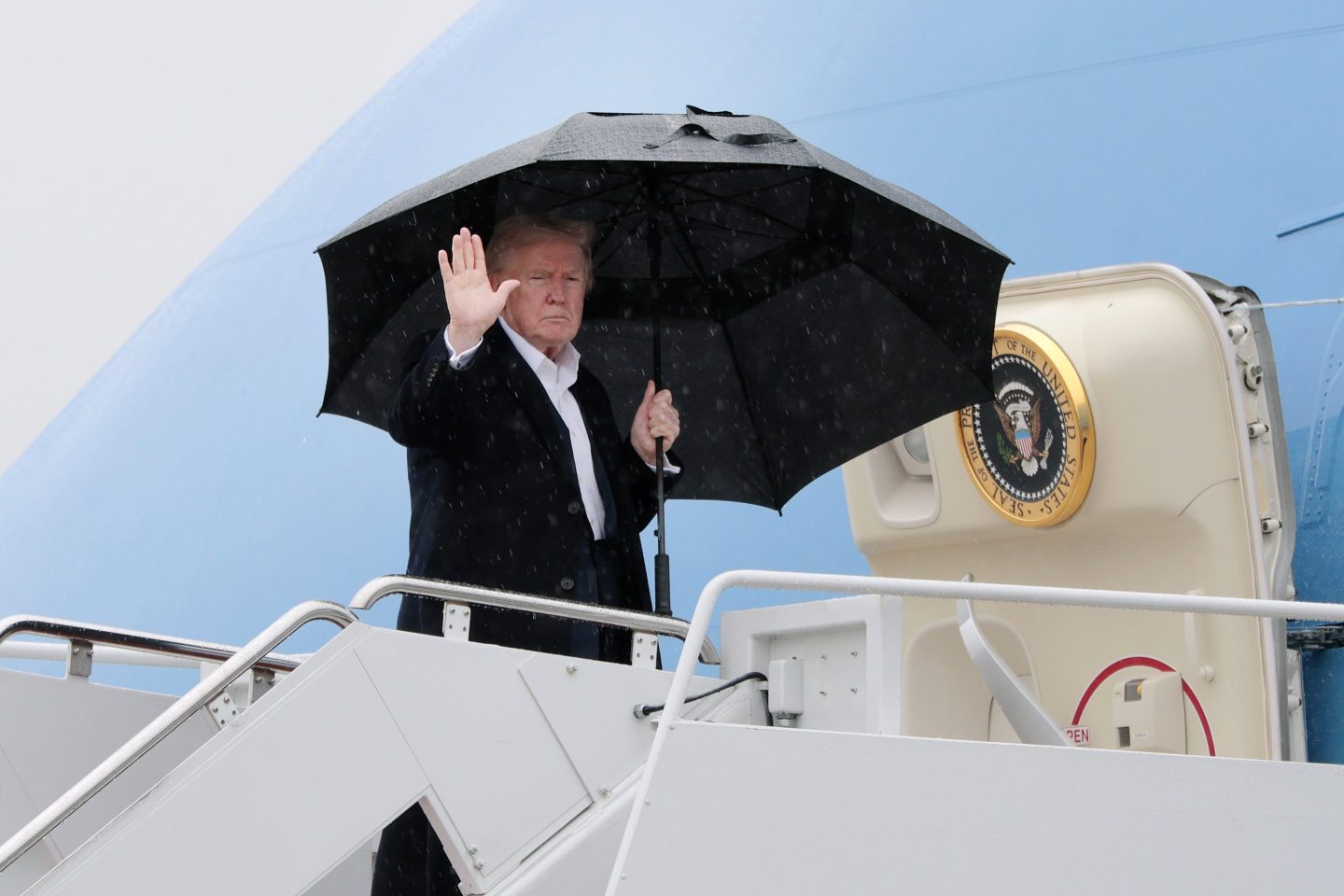 Donald Trump, holding a black umbrella, boards Air Force One.